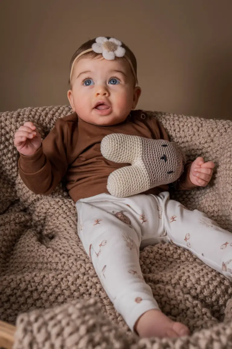 Baby met haarband en gehaakte konijn knuffel in stoel, zachte babykleding in neutrale kleuren